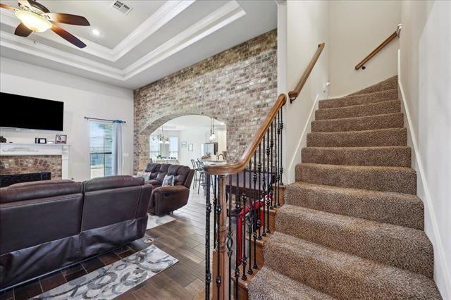 living area with ceiling fan, visible vents, stairs, wood finished floors, and arched walkways