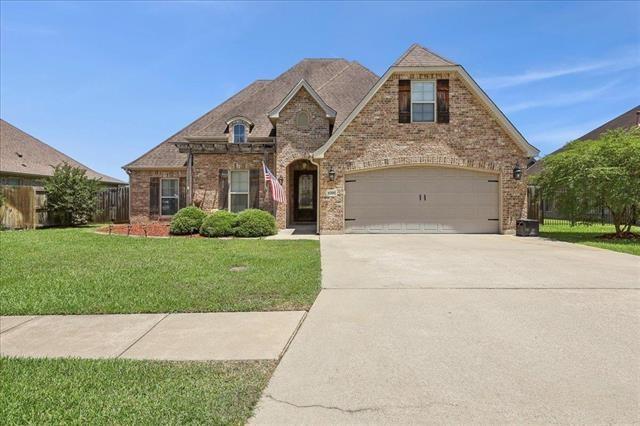french country inspired facade with fence, driveway, brick siding, and a front yard