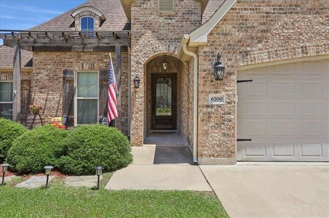 view of exterior entry with a pergola, concrete driveway, an attached garage, and brick siding