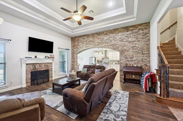 living room featuring a tray ceiling, wood finished floors, a ceiling fan, and a fireplace