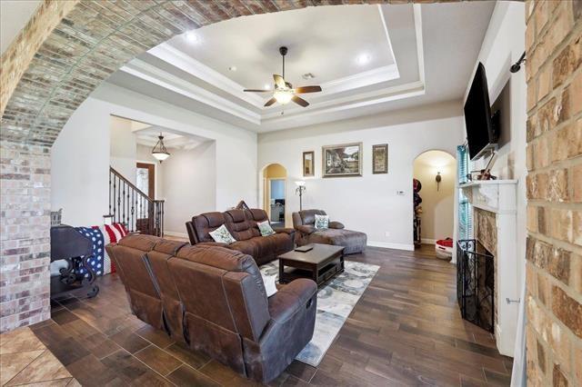 living area featuring stairs, a fireplace, arched walkways, a ceiling fan, and a tray ceiling