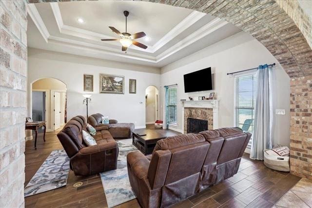 living area featuring a fireplace, a raised ceiling, ceiling fan, and arched walkways
