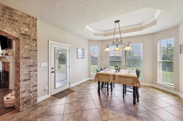 tiled dining space featuring a tray ceiling, crown molding, baseboards, and a brick fireplace