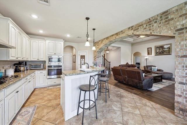 kitchen with a breakfast bar, open floor plan, light stone countertops, arched walkways, and appliances with stainless steel finishes