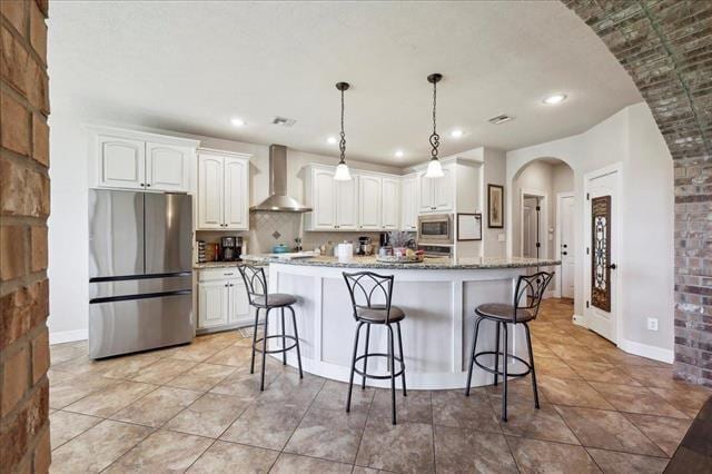 kitchen with wall chimney range hood, a kitchen breakfast bar, white cabinets, and appliances with stainless steel finishes