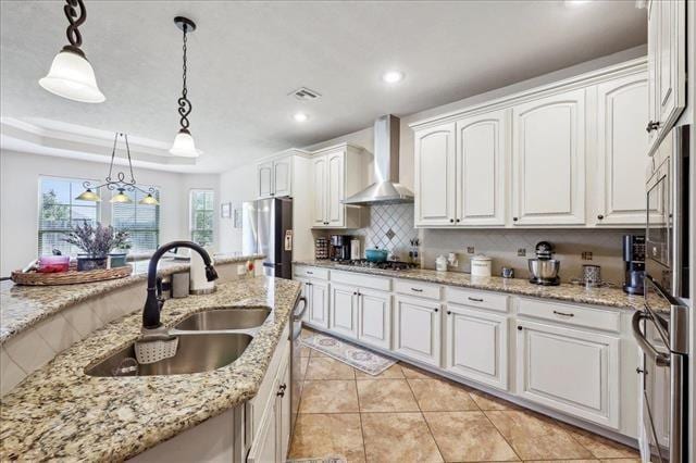 kitchen featuring a sink, white cabinetry, decorative light fixtures, wall chimney range hood, and appliances with stainless steel finishes