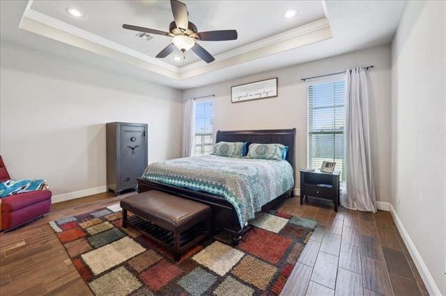bedroom with wood finished floors, a tray ceiling, visible vents, baseboards, and ornamental molding