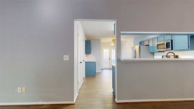 kitchen featuring ceiling fan, wood finished floors, appliances with stainless steel finishes, and blue cabinetry