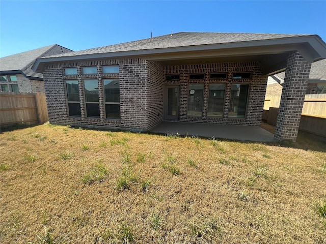back of property with a lawn, a patio, brick siding, and a fenced backyard