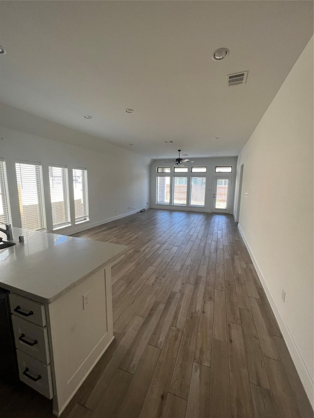 unfurnished living room featuring ceiling fan, baseboards, dark wood-type flooring, and visible vents