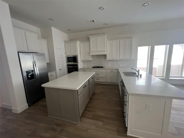 kitchen with a peninsula, a sink, stainless steel appliances, visible vents, and a kitchen island