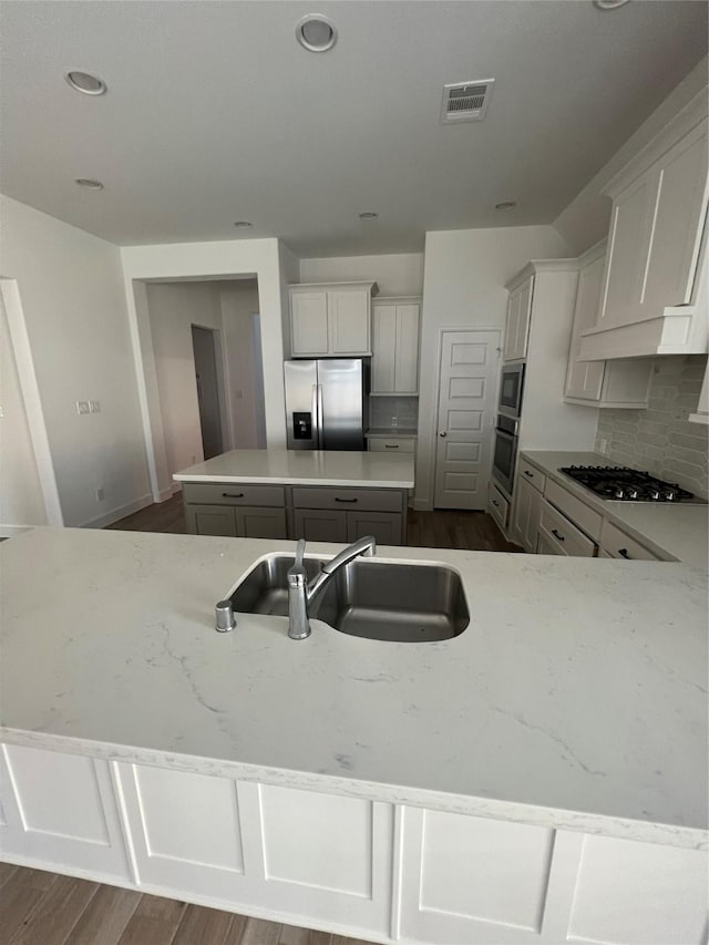 kitchen with a sink, a kitchen island, backsplash, stainless steel appliances, and dark wood-style floors
