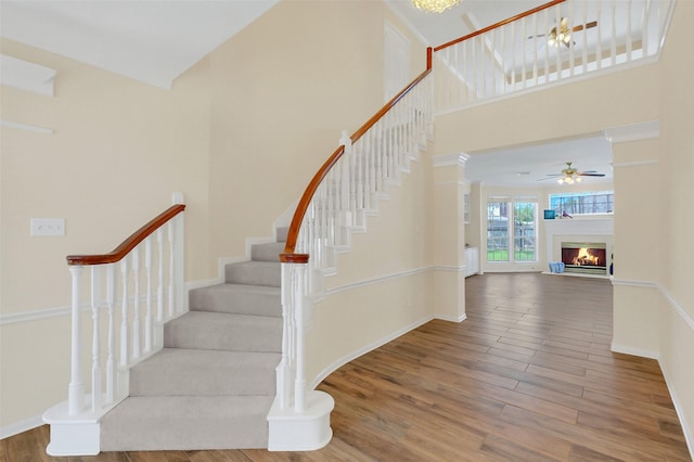 14906 Stonemeade Pl, Cypress, TX 77429 - staircase with wood finished floors, a ceiling fan, a high ceiling, and a glass covered fireplace