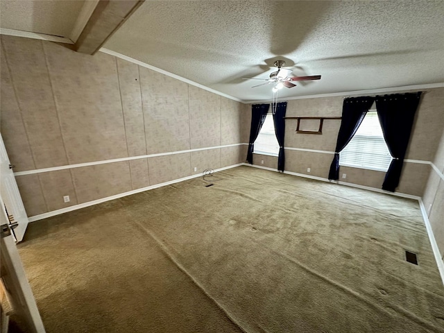 carpeted spare room featuring ornamental molding, a textured ceiling, visible vents, a ceiling fan, and baseboards