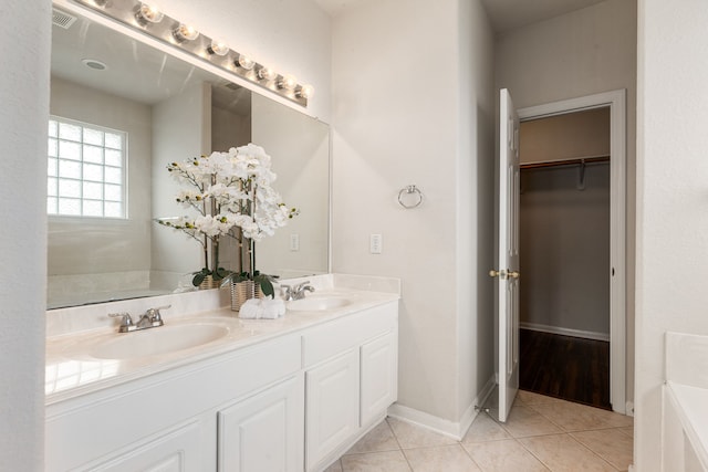 bathroom with tile patterned floors, double vanity, a bath, baseboards, and a spacious closet