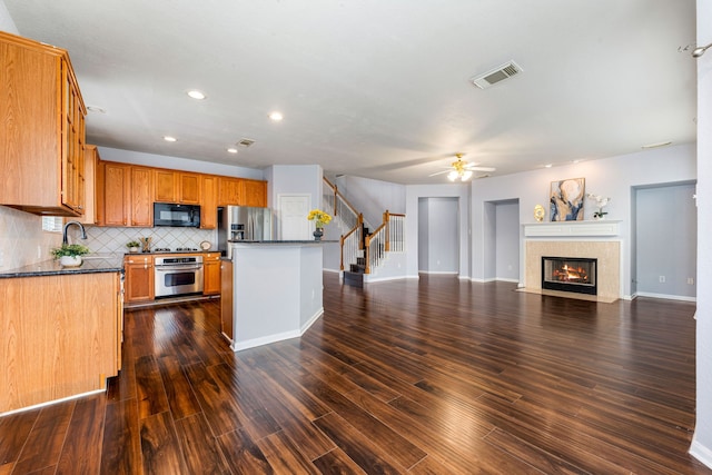 kitchen with appliances with stainless steel finishes, ceiling fan, open floor plan, a tiled fireplace, and backsplash