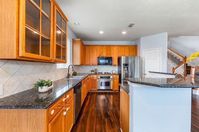 kitchen with stainless steel appliances, a sink, dark wood-style flooring, brown cabinets, and decorative backsplash