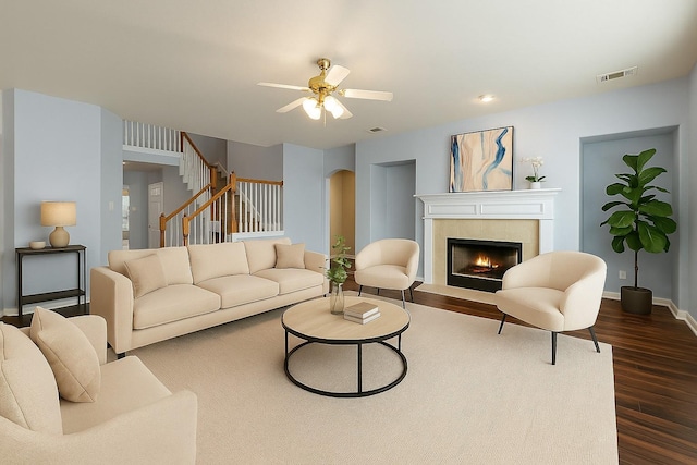 living room featuring dark wood finished floors, a tile fireplace, a ceiling fan, baseboards, and stairs