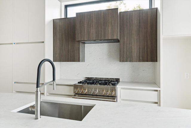 kitchen with dark brown cabinets, modern cabinets, stainless steel stove, a sink, and white cabinetry