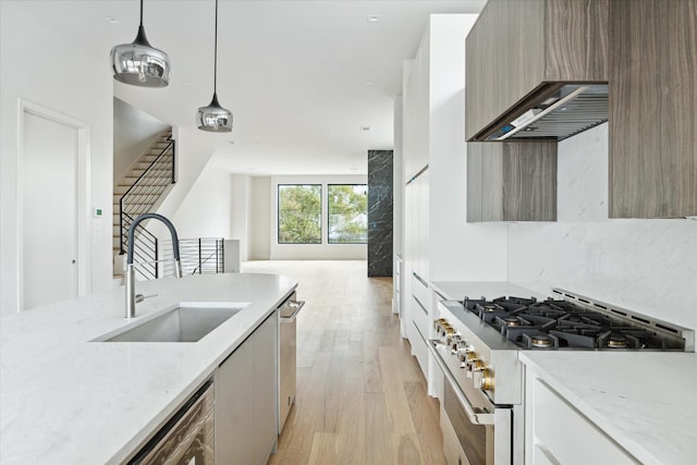 kitchen with a sink, light wood-type flooring, modern cabinets, high end range, and wall chimney range hood