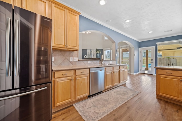 kitchen with appliances with stainless steel finishes, arched walkways, ornamental molding, tasteful backsplash, and light wood-style floors