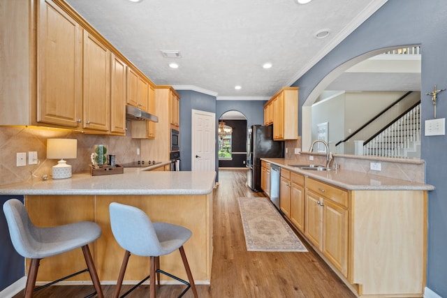kitchen with arched walkways, a peninsula, a sink, black appliances, and under cabinet range hood