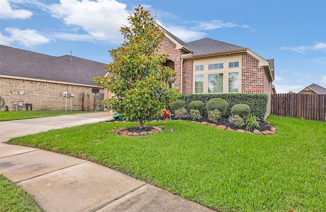 view of front facade with fence, concrete driveway, brick siding, and a front yard