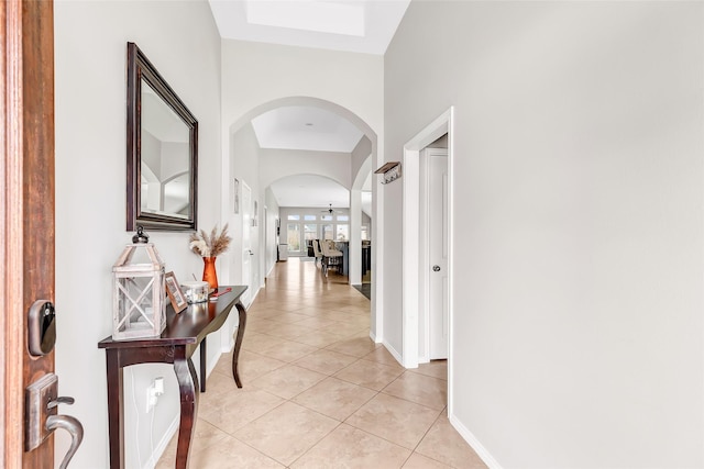 corridor with arched walkways, baseboards, and light tile patterned flooring