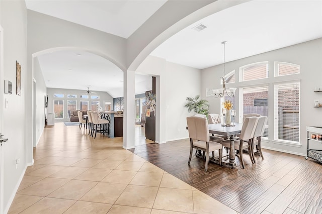 tiled dining space featuring arched walkways, a notable chandelier, visible vents, and baseboards
