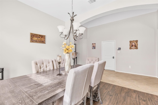 dining room featuring lofted ceiling, a notable chandelier, visible vents, wood finished floors, and arched walkways