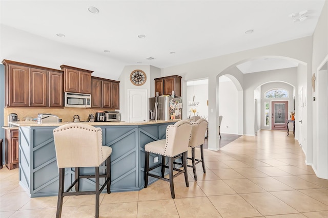kitchen with backsplash, arched walkways, light countertops, light tile patterned floors, and appliances with stainless steel finishes
