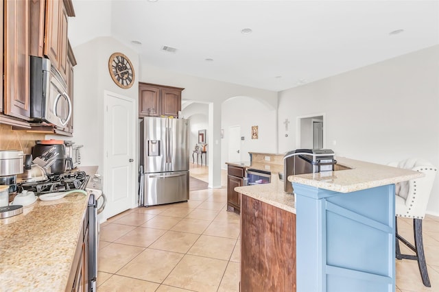 kitchen featuring light tile patterned floors, a breakfast bar, stainless steel appliances, visible vents, and arched walkways