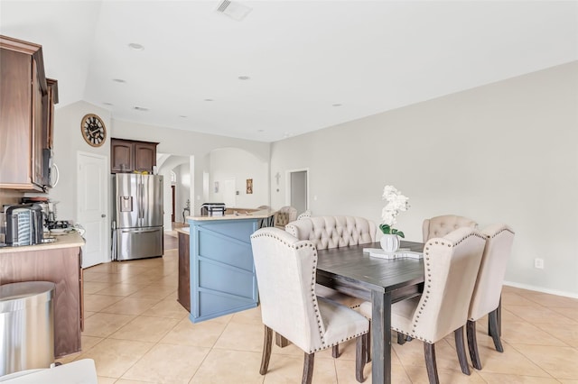 dining room featuring light tile patterned floors, visible vents, lofted ceiling, and arched walkways