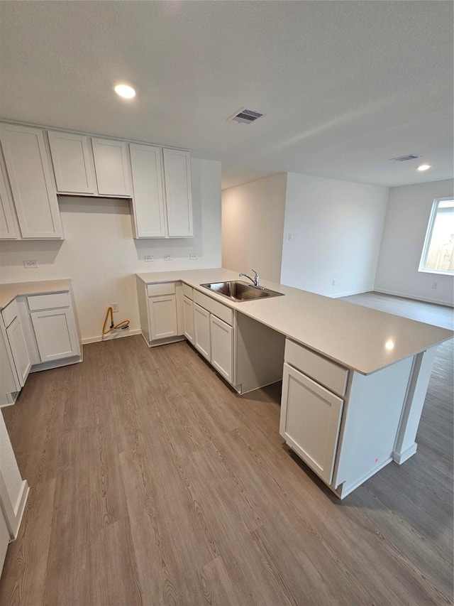 kitchen featuring a sink, a peninsula, wood finished floors, visible vents, and white cabinets