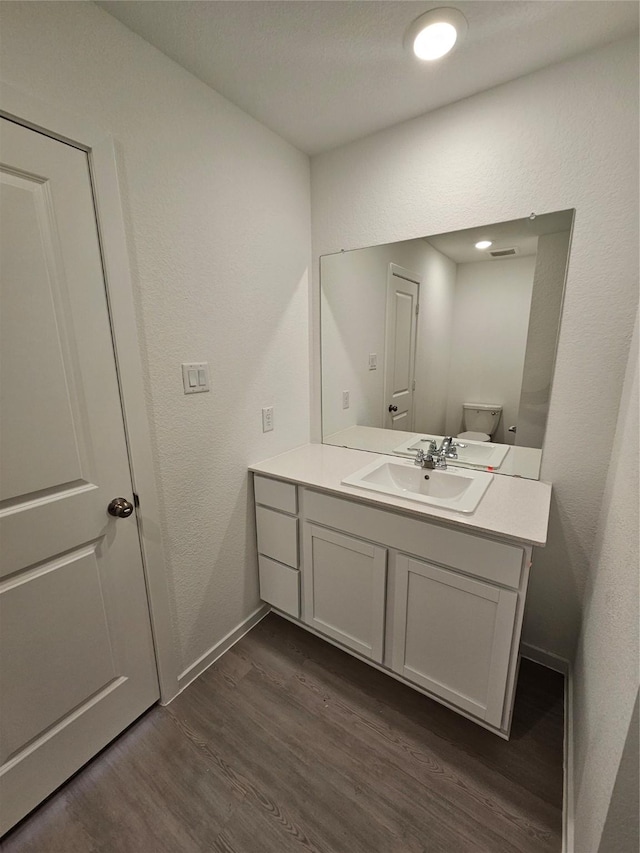 bathroom featuring toilet, wood finished floors, vanity, a textured wall, and baseboards