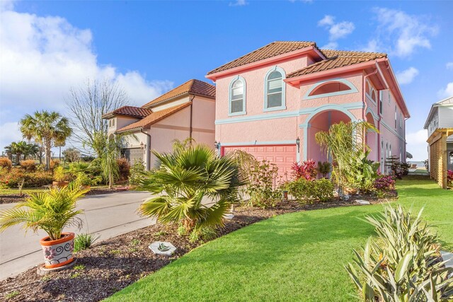 mediterranean / spanish-style home featuring a tile roof, stucco siding, a garage, and a front lawn