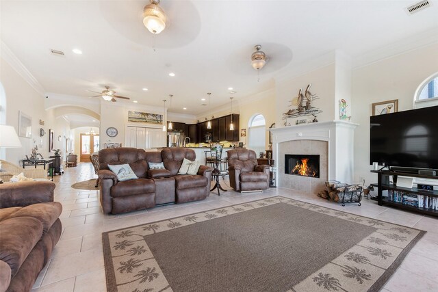 living area featuring visible vents, crown molding, arched walkways, a ceiling fan, and light tile patterned floors
