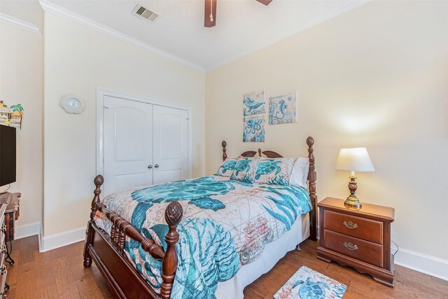 bedroom featuring a closet, baseboards, ornamental molding, visible vents, and wood finished floors