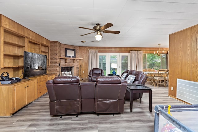 living area featuring light wood-style floors, a healthy amount of sunlight, wood walls, and ceiling fan with notable chandelier