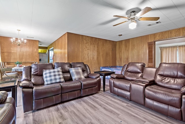 cinema featuring visible vents, light wood-style flooring, ceiling fan with notable chandelier, and wooden walls