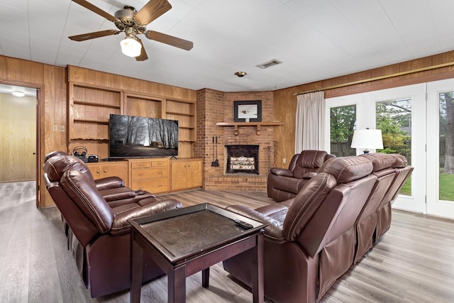 living room featuring ceiling fan, visible vents, a brick fireplace, wood walls, and light wood-type flooring