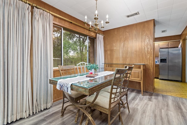dining area featuring light wood-style flooring, a notable chandelier, wooden walls, and visible vents