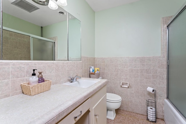 full bathroom with tile walls, toilet, shower / bath combination with glass door, vanity, and a wainscoted wall
