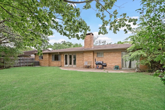 rear view of house featuring central AC, fence, a chimney, a lawn, and brick siding