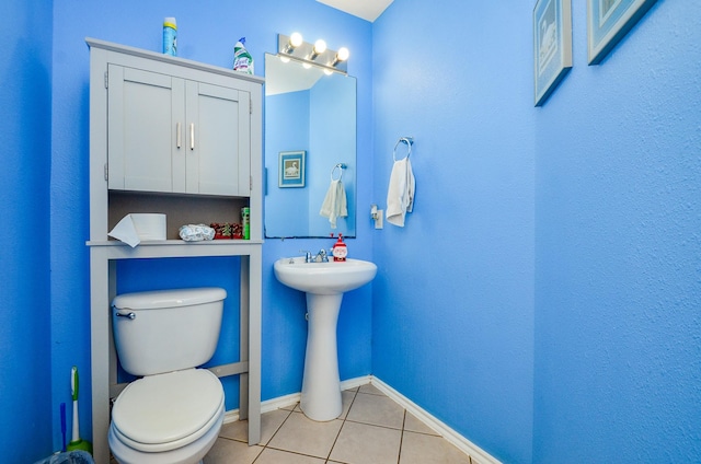 half bath with tile patterned floors, toilet, baseboards, and a sink