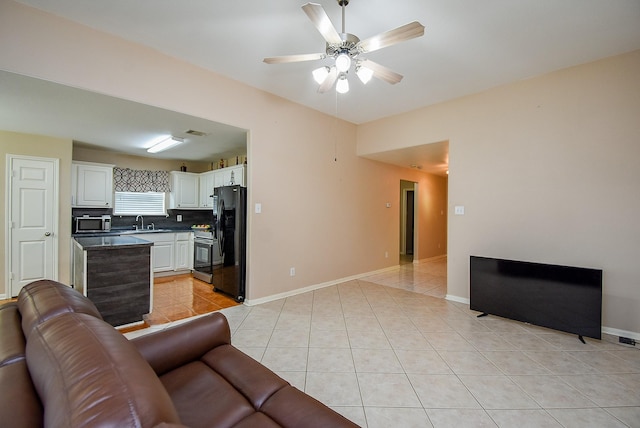 living area featuring light tile patterned floors, a ceiling fan, and baseboards