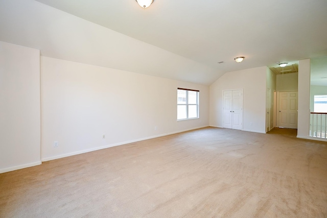 unfurnished room featuring light colored carpet, attic access, vaulted ceiling, and baseboards