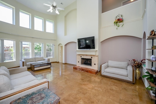 living room featuring a fireplace, ceiling fan, a towering ceiling, and arched walkways