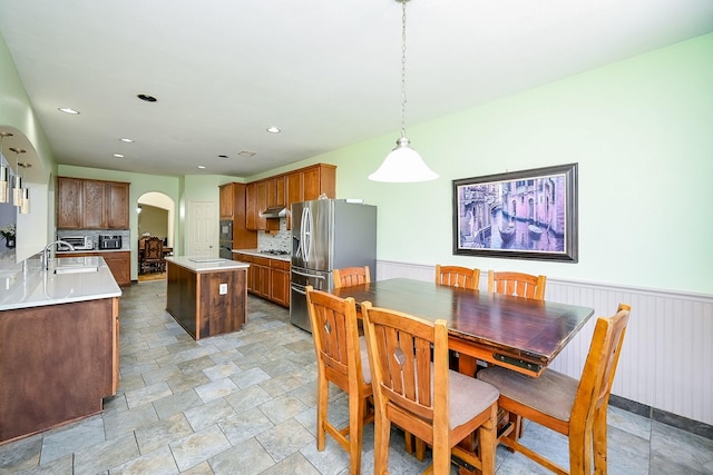 dining space featuring arched walkways, stone finish flooring, recessed lighting, and a wainscoted wall