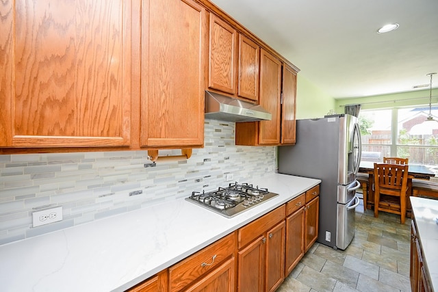 kitchen with under cabinet range hood, brown cabinets, backsplash, and appliances with stainless steel finishes
